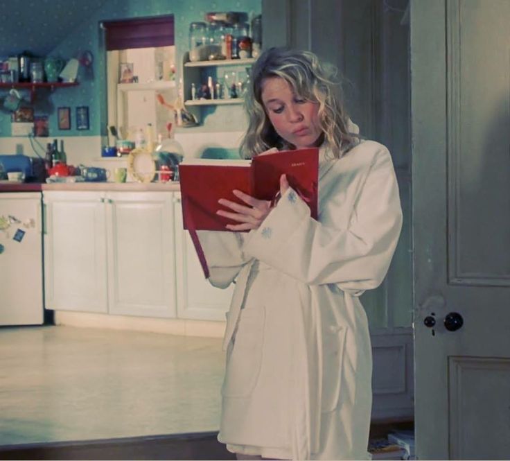 a woman standing in a kitchen holding a red binder and looking at the camera