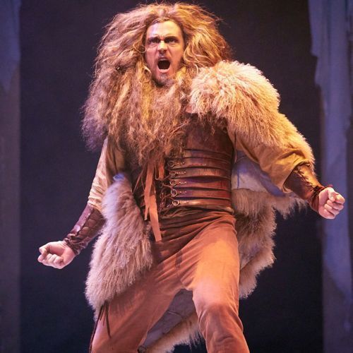 a man with long hair is dressed in costume and has his mouth open while standing on stage