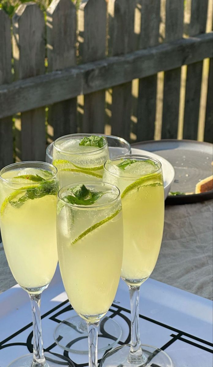 three glasses filled with drinks sitting on top of a white table next to a wooden fence