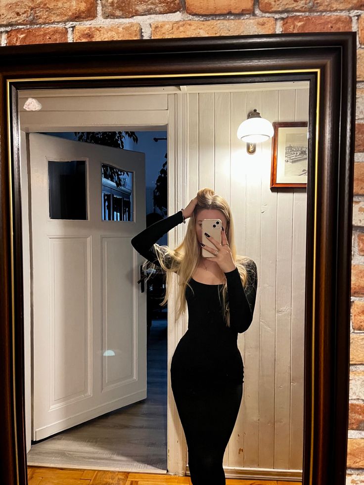 a woman taking a selfie in front of a mirror wearing a black bodysuit