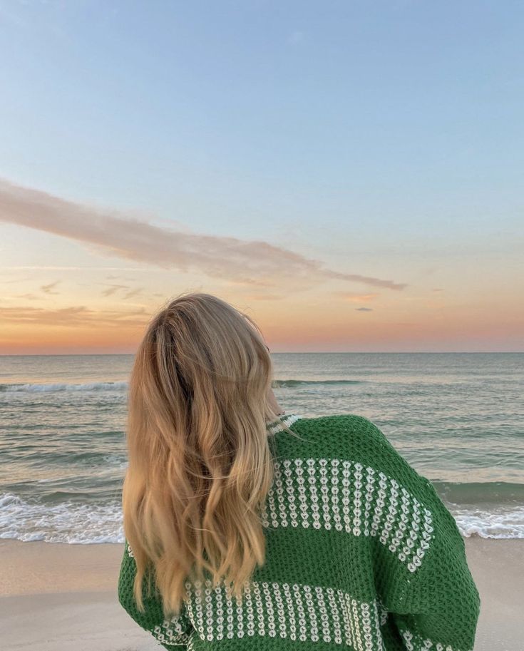 a woman standing on top of a sandy beach next to the ocean at sunset or dawn