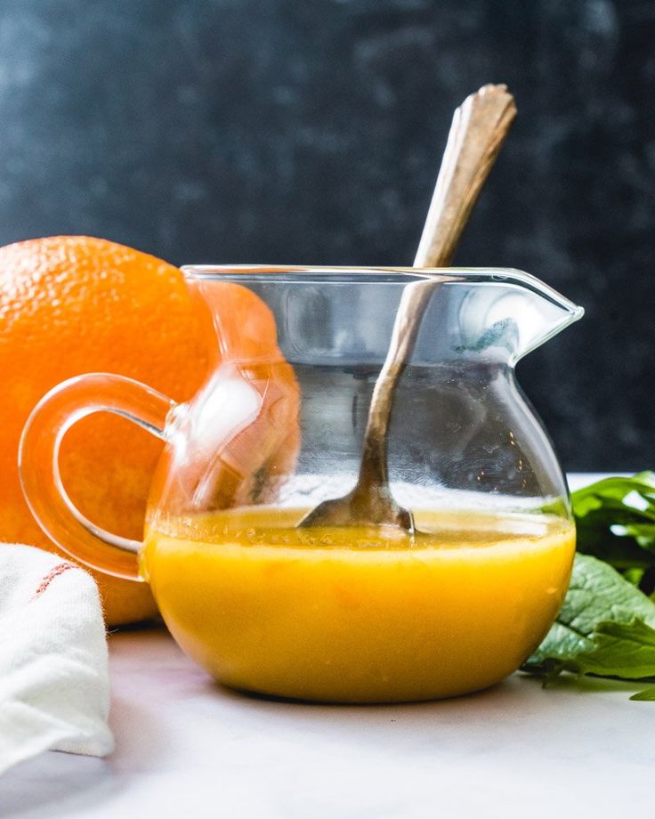 an orange juice in a glass pitcher with a wooden spoon next to it on a table