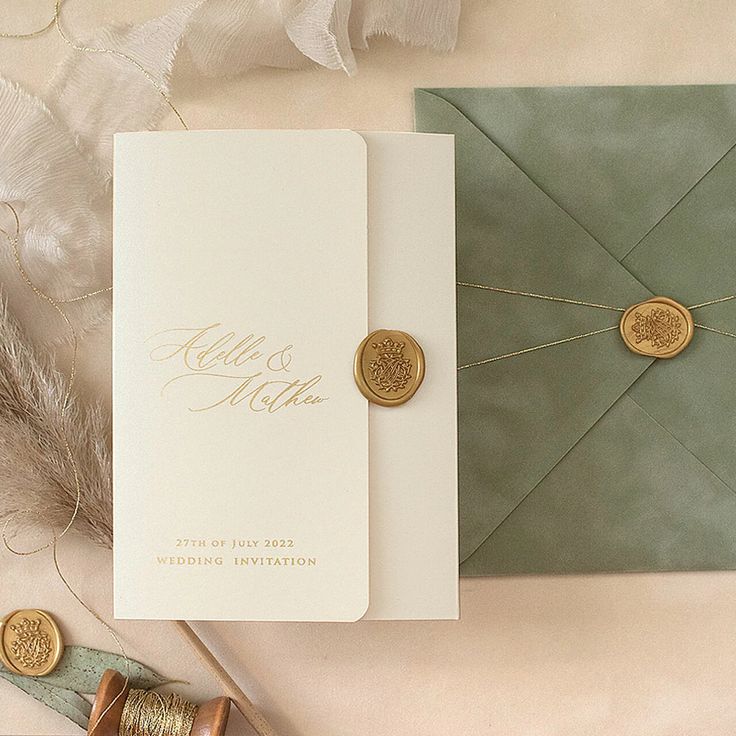 an envelope with two gold buttons on it next to a feather and some other items