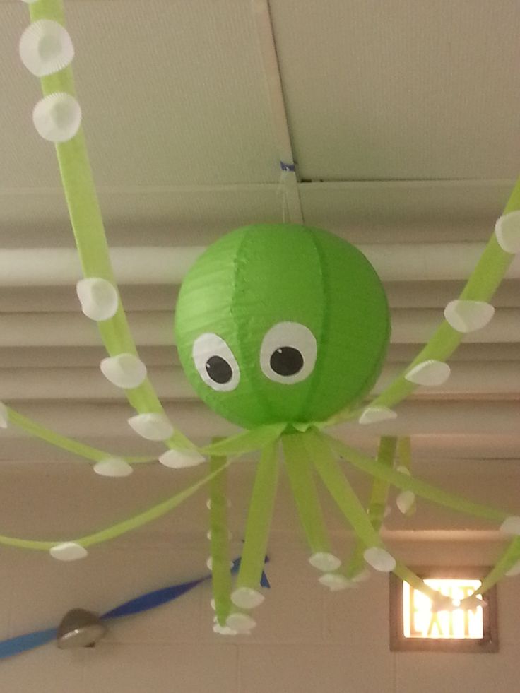 a green paper lantern hanging from the ceiling with googly eyes on it's legs