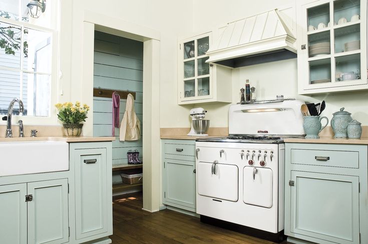 an old fashioned kitchen with white appliances and blue cabinets in the center, along with wood flooring