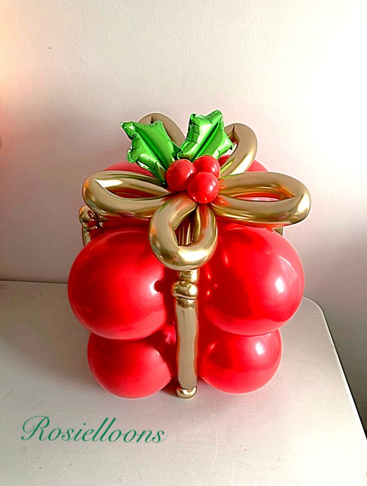 a red balloon wrapped in gold and green ribbon with a bow on the handle is sitting on a white surface