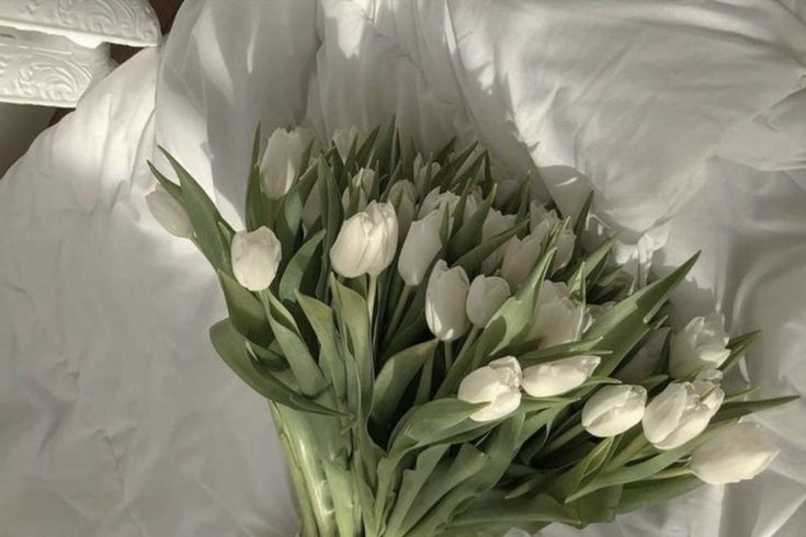 a bouquet of white tulips in a vase on a bed sheeted surface