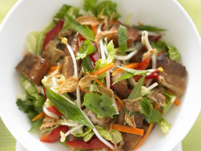 a white bowl filled with salad and meat on top of a green tablecloth covered table