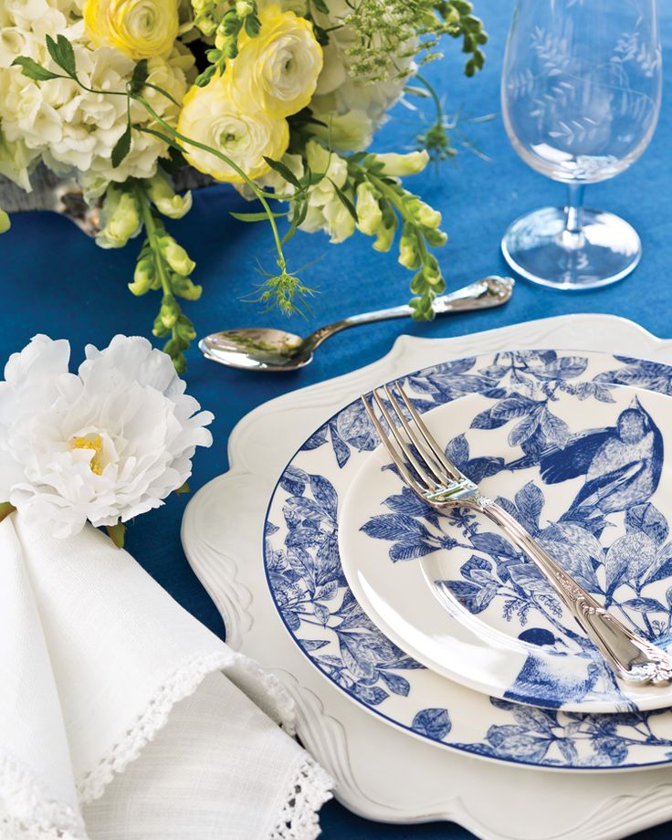 a blue and white place setting with flowers on the side, silverware and napkins