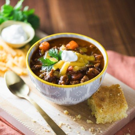 a bowl of chili with sour cream on top next to some bread and other food