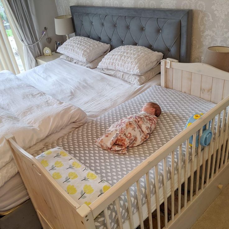 a baby laying on top of a white crib next to a bed with pillows