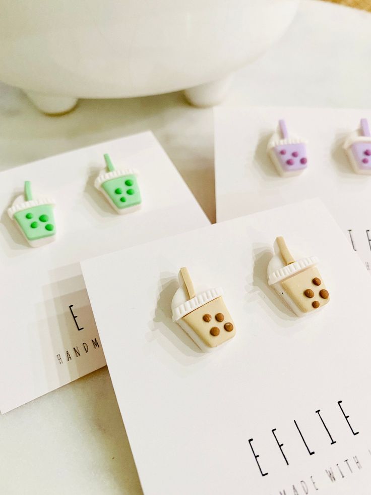 three pairs of earrings sitting on top of a card next to a white vase and cup