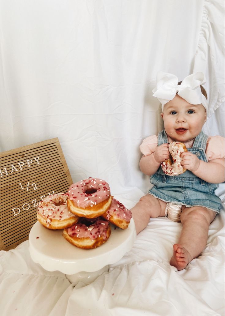 a baby sitting on a bed next to a plate of doughnuts and a sign that says happy birthday