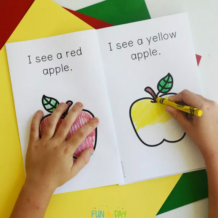 a child's hands holding a crayon and writing on an apple book