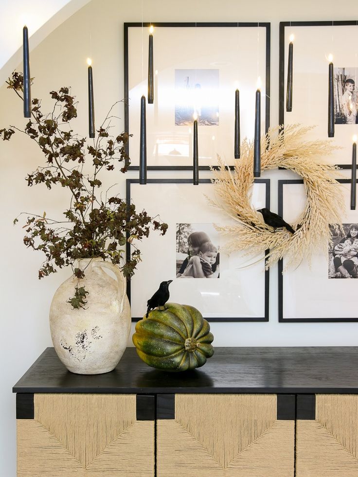 two vases with plants on top of a black and white dresser next to pictures