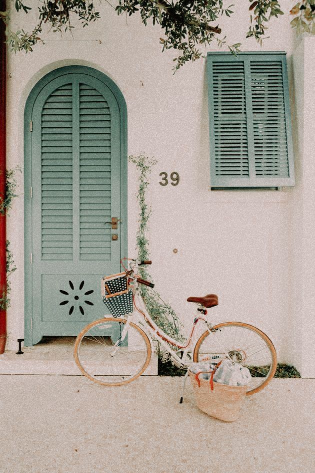 a bicycle parked in front of a blue door and shutters on a white building