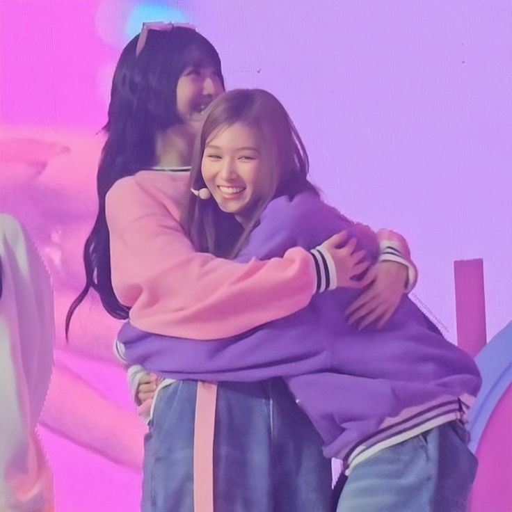 two girls hugging each other in front of a pink background