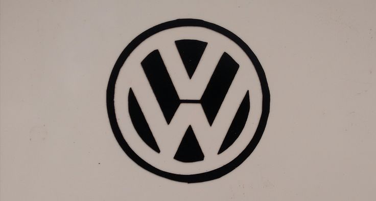 a volkswagen logo is shown on the side of a white wall with black letters and an arrow in the center