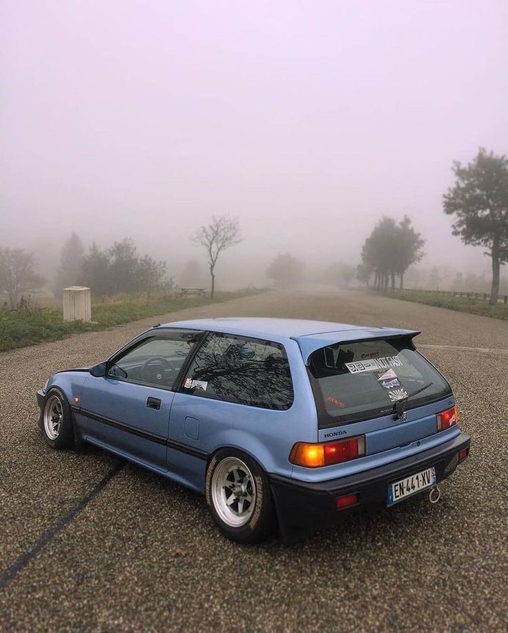 a blue car parked in the middle of a parking lot on a foggy day