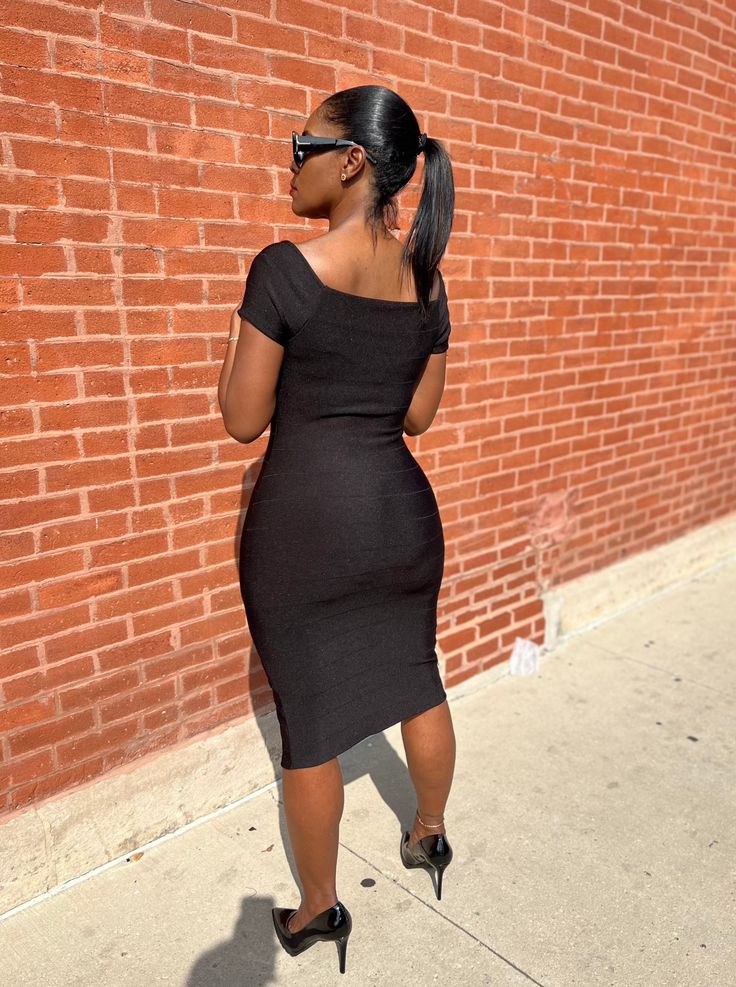 a woman in a black dress is leaning against a brick wall