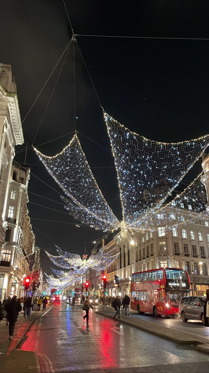 people are walking down the street in front of buildings with christmas lights strung across them