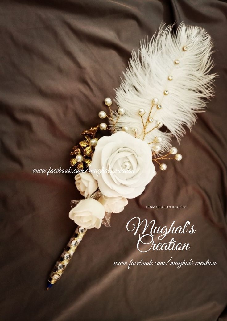 a white rose and feather boutonniere on a brown satin background with the words maggod's creation written below it