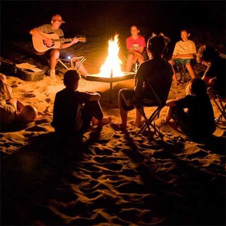 people sitting around a campfire at night on the beach with guitars and guitar players