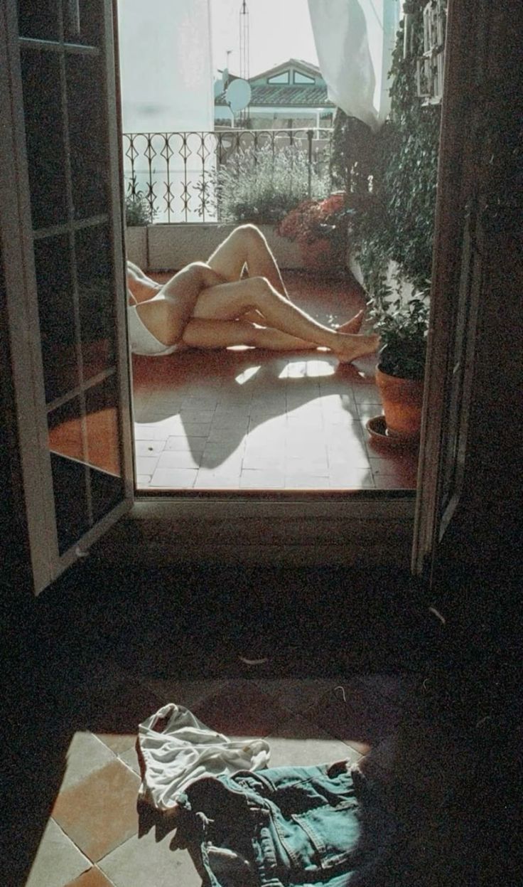 a naked woman laying on the floor in front of an open door to a balcony