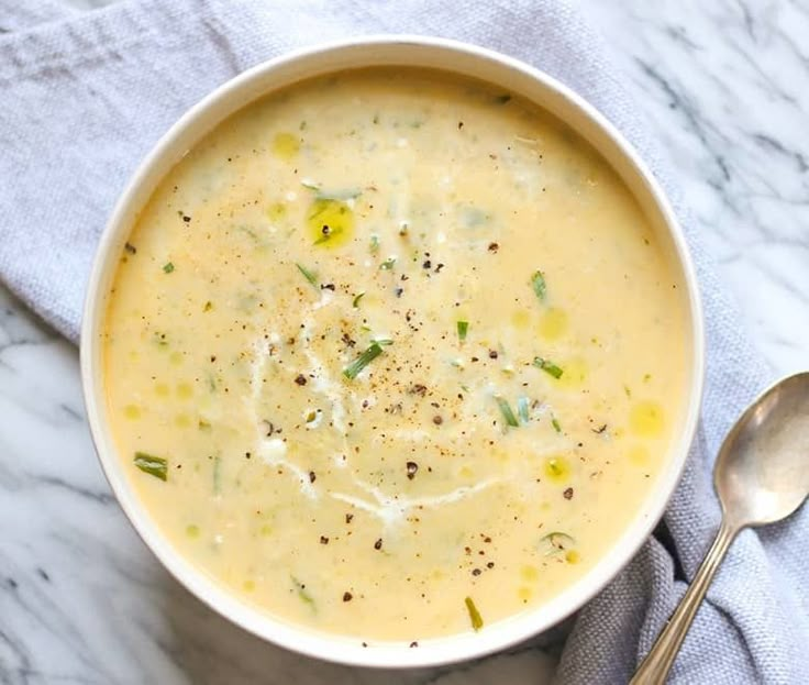 a white bowl filled with soup on top of a blue towel next to a spoon