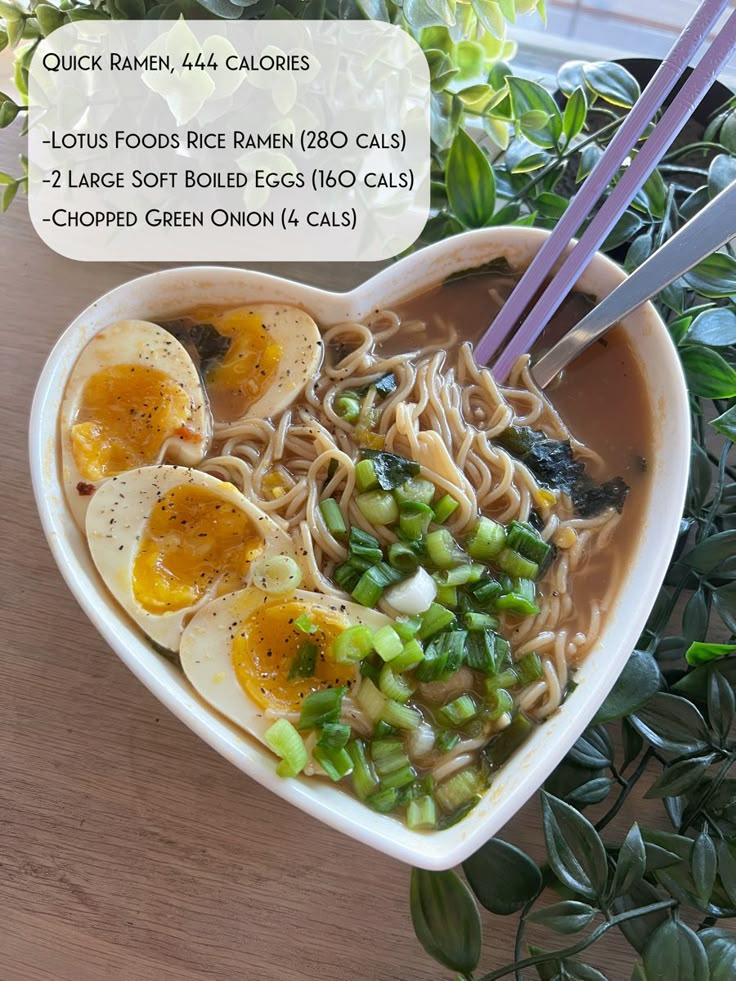 a heart shaped bowl filled with noodles and vegetables next to chopsticks on a table