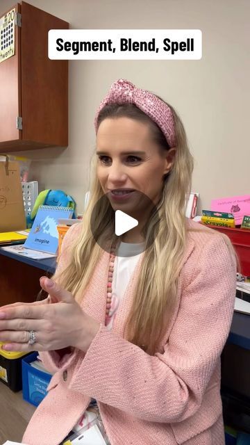 a woman with long blonde hair wearing a pink sweater and headband talking to someone