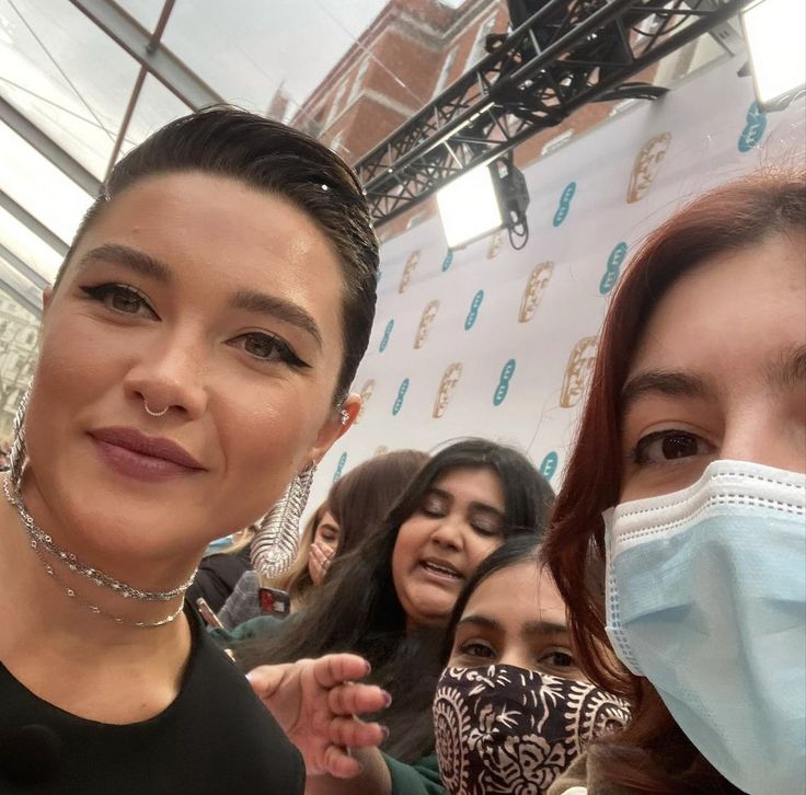 two women wearing face masks and posing for the camera with other people in the background