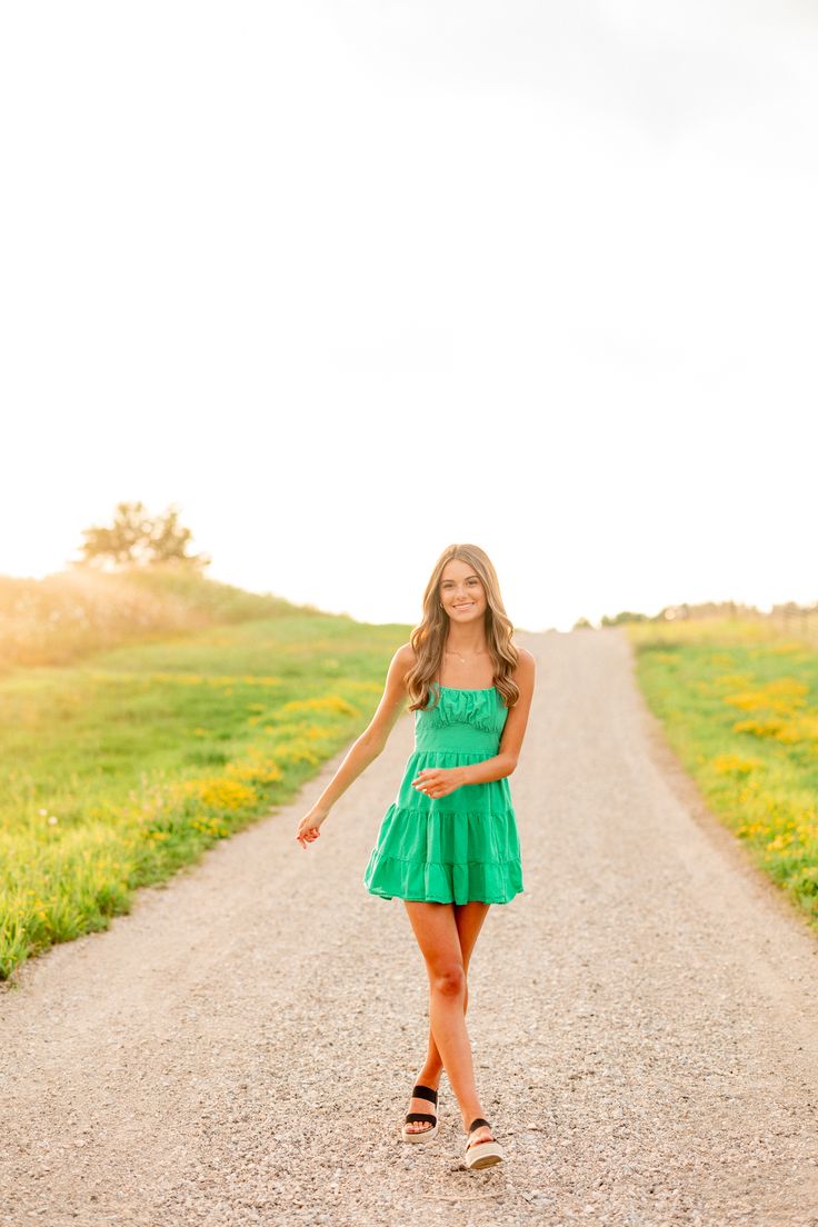 a woman in a green dress is standing on a dirt road and smiling at the camera