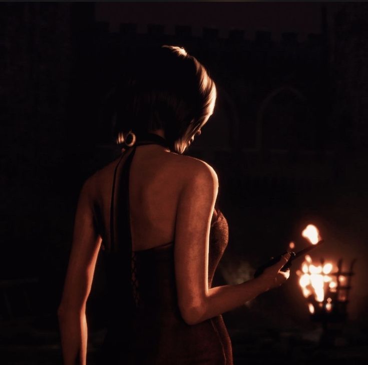 a woman in a red dress holding a lit candle and looking at the ground with her back to the camera