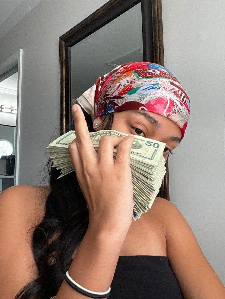 a woman with a bandana covering her face and holding money in front of her face