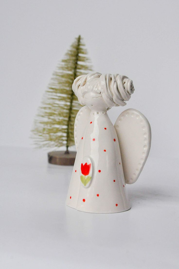 a white ceramic angel ornament next to a small christmas tree