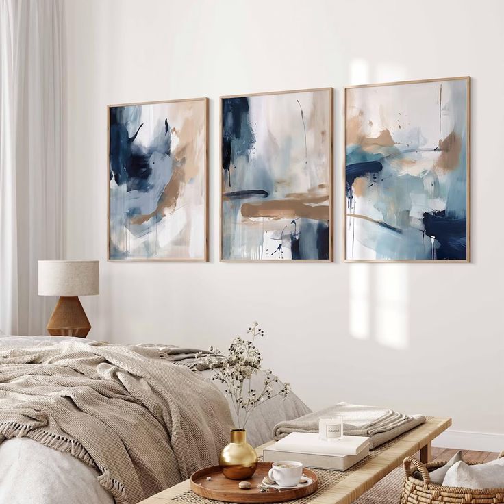 three paintings hanging on the wall above a bed in a room with a wooden coffee table