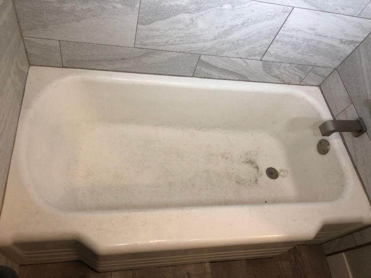 a dirty bathtub in the middle of a tiled floored bathroom with no shower curtain