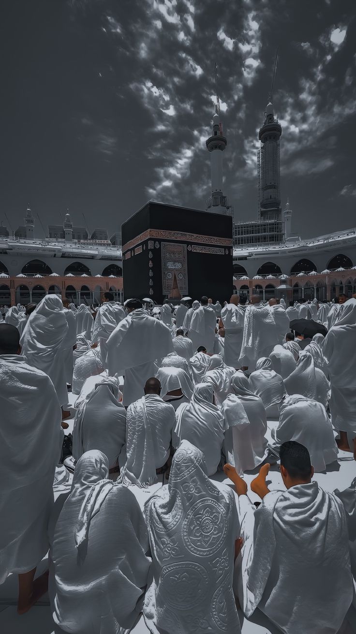 a group of people in white robes sitting on the ground near a building with a sky background