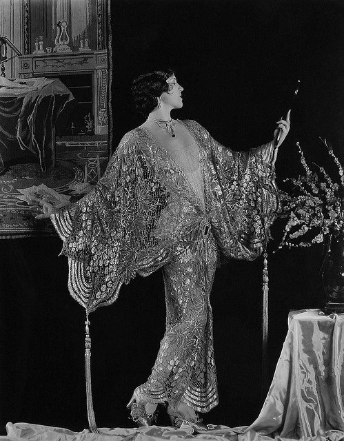 an old fashion photo of a woman standing in front of a table with flowers on it