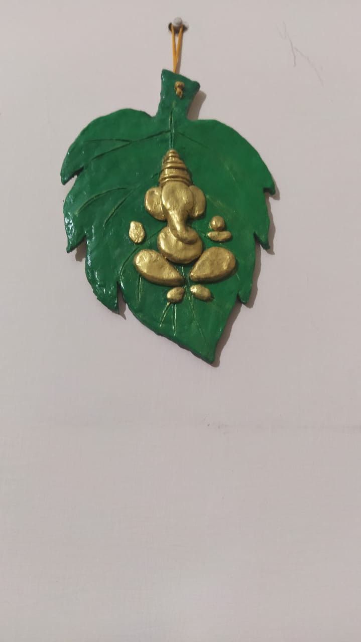 a green and gold leaf shaped ornament hanging on a wall with an elephant