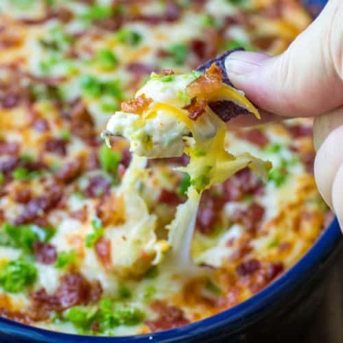 a hand holding a piece of broccoli and cheese casserole in a blue dish