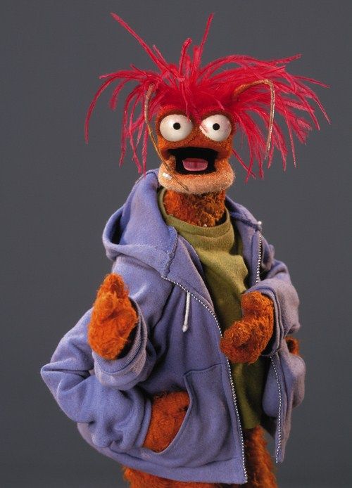 an orange stuffed animal with red hair wearing a blue jacket and green hoodie standing in front of a gray background