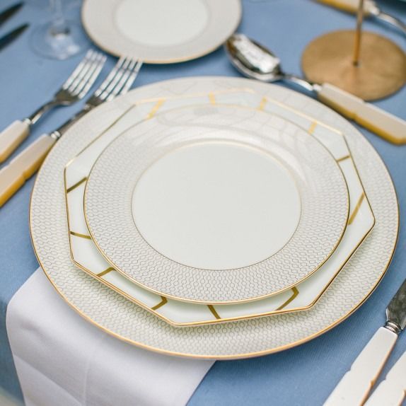 the table is set with white and gold plates, silverware, and napkins