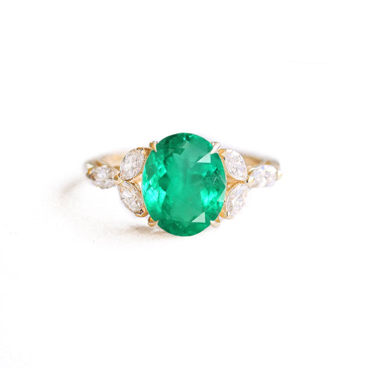 an oval emerald and diamond ring on a white background with the center stone in yellow gold