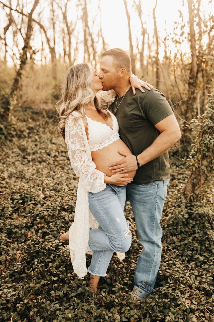 a pregnant couple kissing in the woods