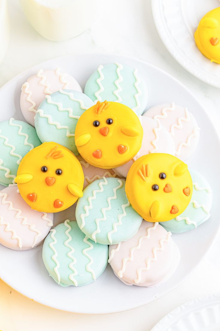 several decorated cookies on a white plate with yellow and blue ones in the shape of chicks