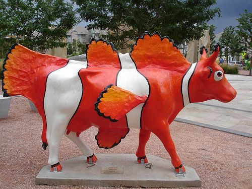 a red and white cow statue sitting on top of a cement slab next to a tree