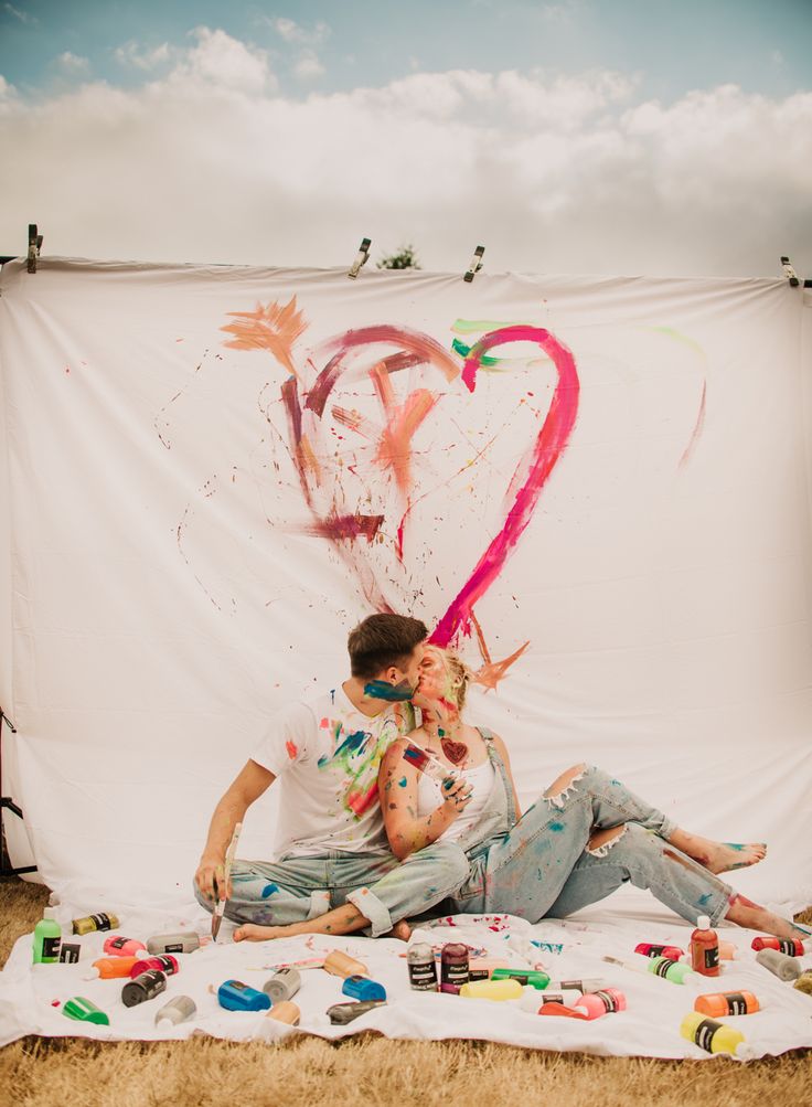 a man and woman sitting on the ground in front of a backdrop with hearts painted on it