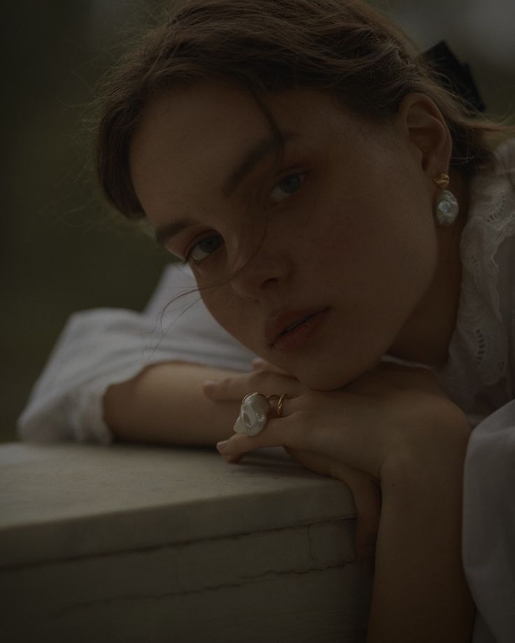 a woman leaning against a wall with her hand on her chin